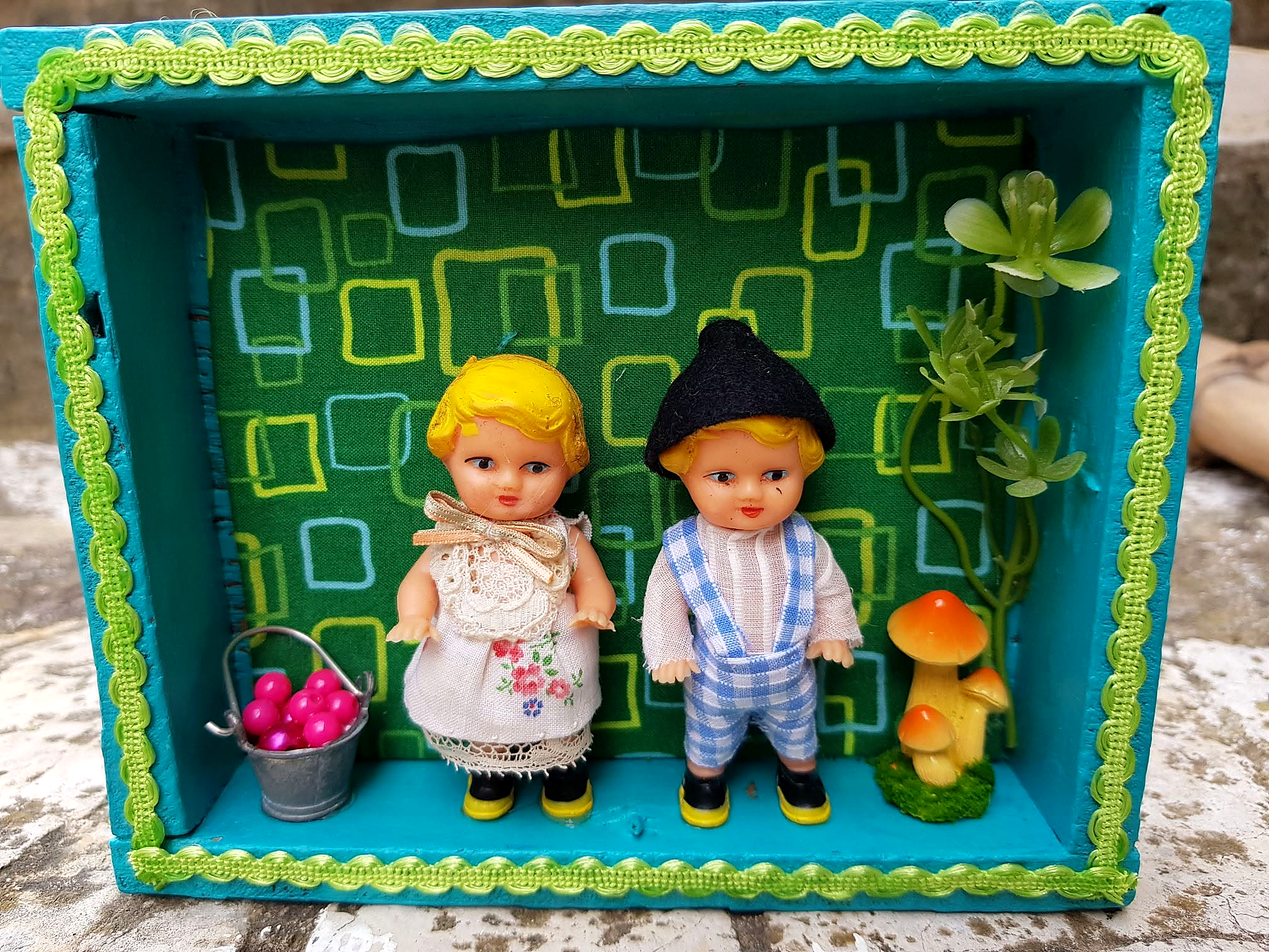 Deux dioramas miniatures avec des poupées ARI — créations de Sylvie — Vitrine turquoise créée par Sylvie, avec deux petites poupées présentées comme des ARI, un seau miniature et des champignons décoratifs — vue 1.