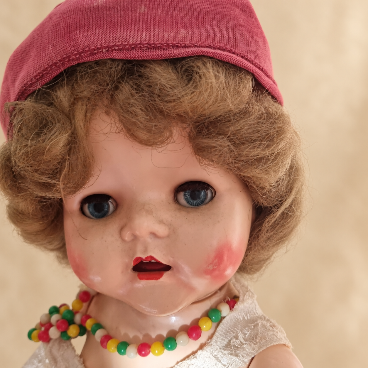 Poupées Pedigree — collection de Marie — Gros plan du visage : yeux bleus, boucles châtain clair, bonnet rouge et collier de perles multicolores — vue 3.