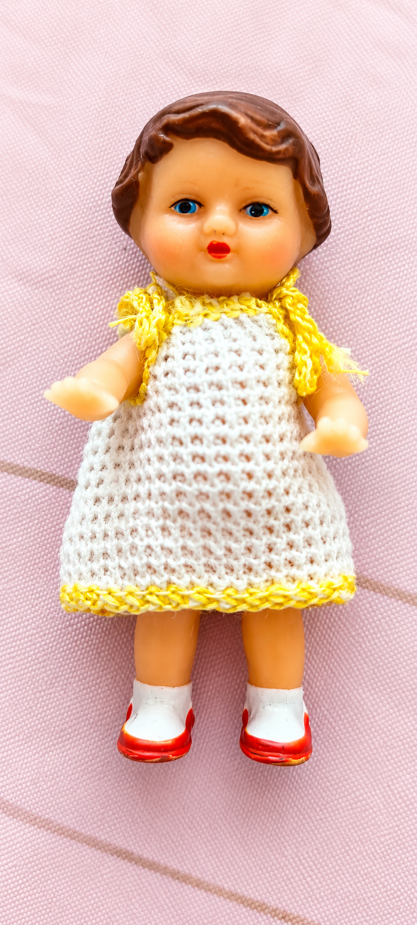 Poupée ARI en robe crochetée blanche et jaune — collection d’Anisabel — Poupée ARI de la collection d’Anisabel, en robe crochetée blanche bordée de jaune, photographiée sur un tissu rose — vue 1.