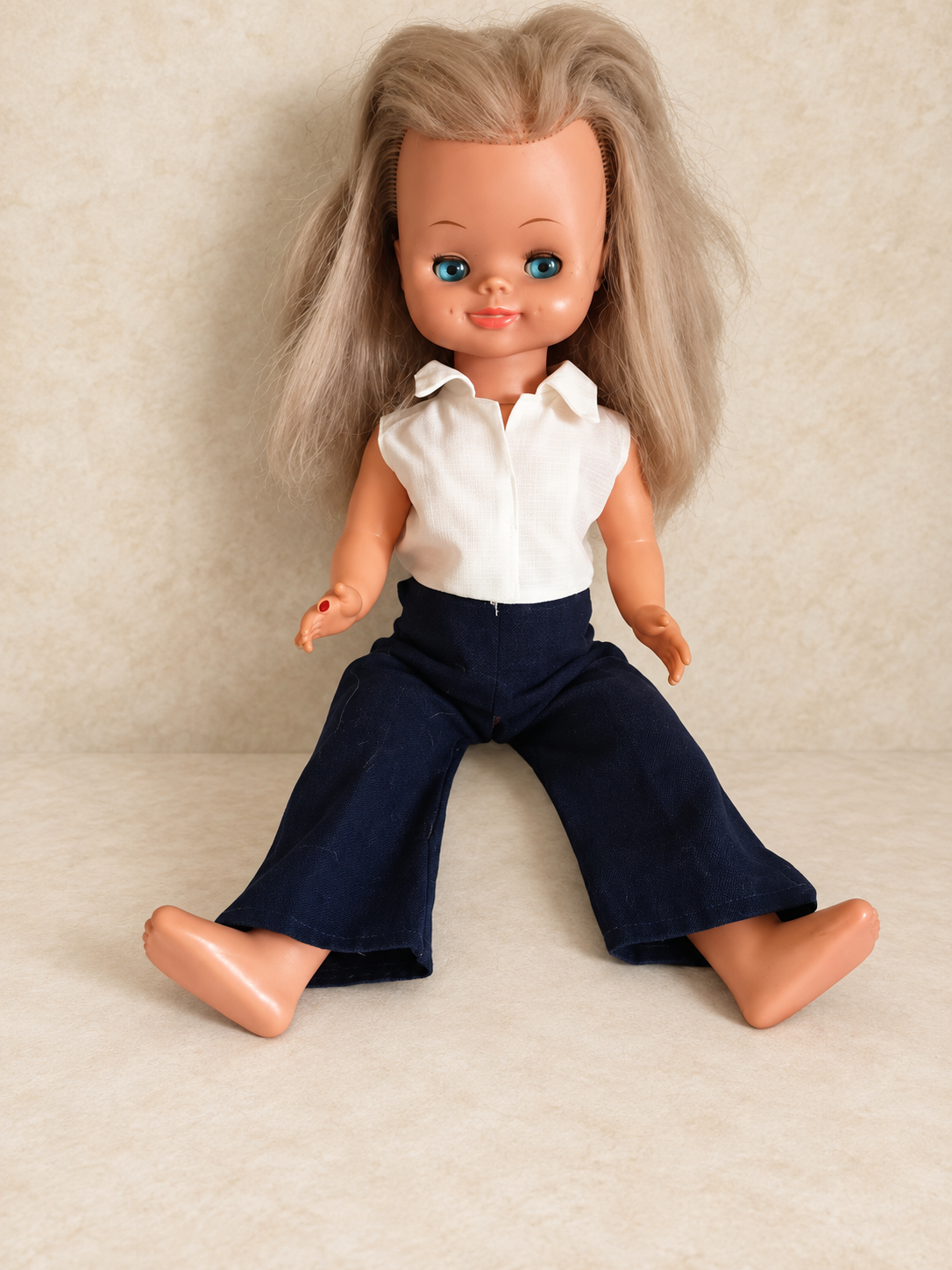 « Delphine », poupée Bella — collection de Sylvie — La « Delphine » de Sylvie, poupée attribuée à Bella par sa propriétaire, aux longs cheveux blonds et aux yeux bleus, portant un chemisier blanc sans manches et un pantalon bleu marine évasé, assise pieds nus — vue 1.