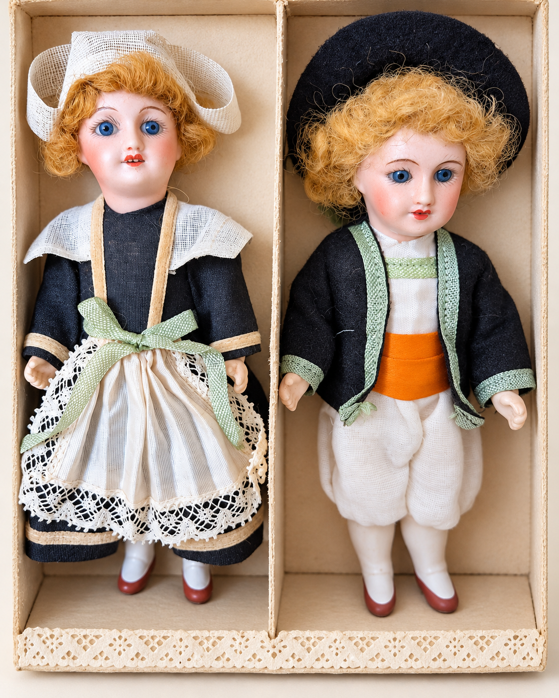 Mignonnettes anciennes : costumes et portraits — collection de Mireille (2/3) — Deux mignonnettes aux cheveux blond-roux dans une boîte compartimentée, en costumes noirs et clairs à galons — vue 1.