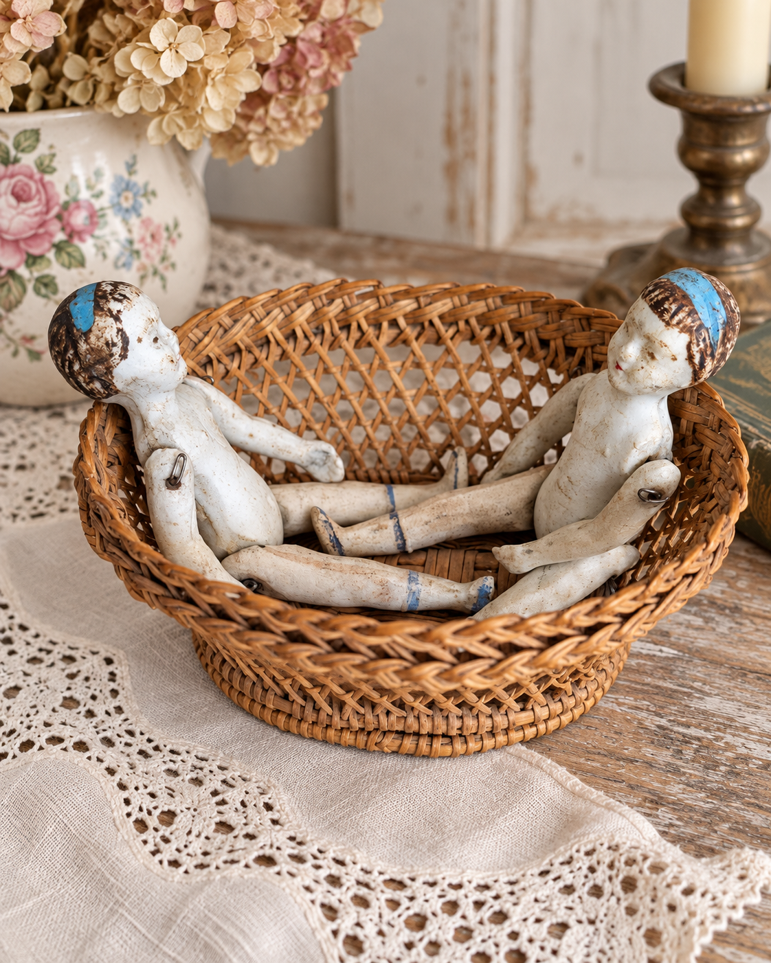 Mignonnettes anciennes et leurs petits accessoires — collection de Mireille (1/3) — Deux petites poupées aux cheveux peints et bandeaux bleus, assises face à face dans un panier tressé ; attaches métalliques visibles — vue 3.