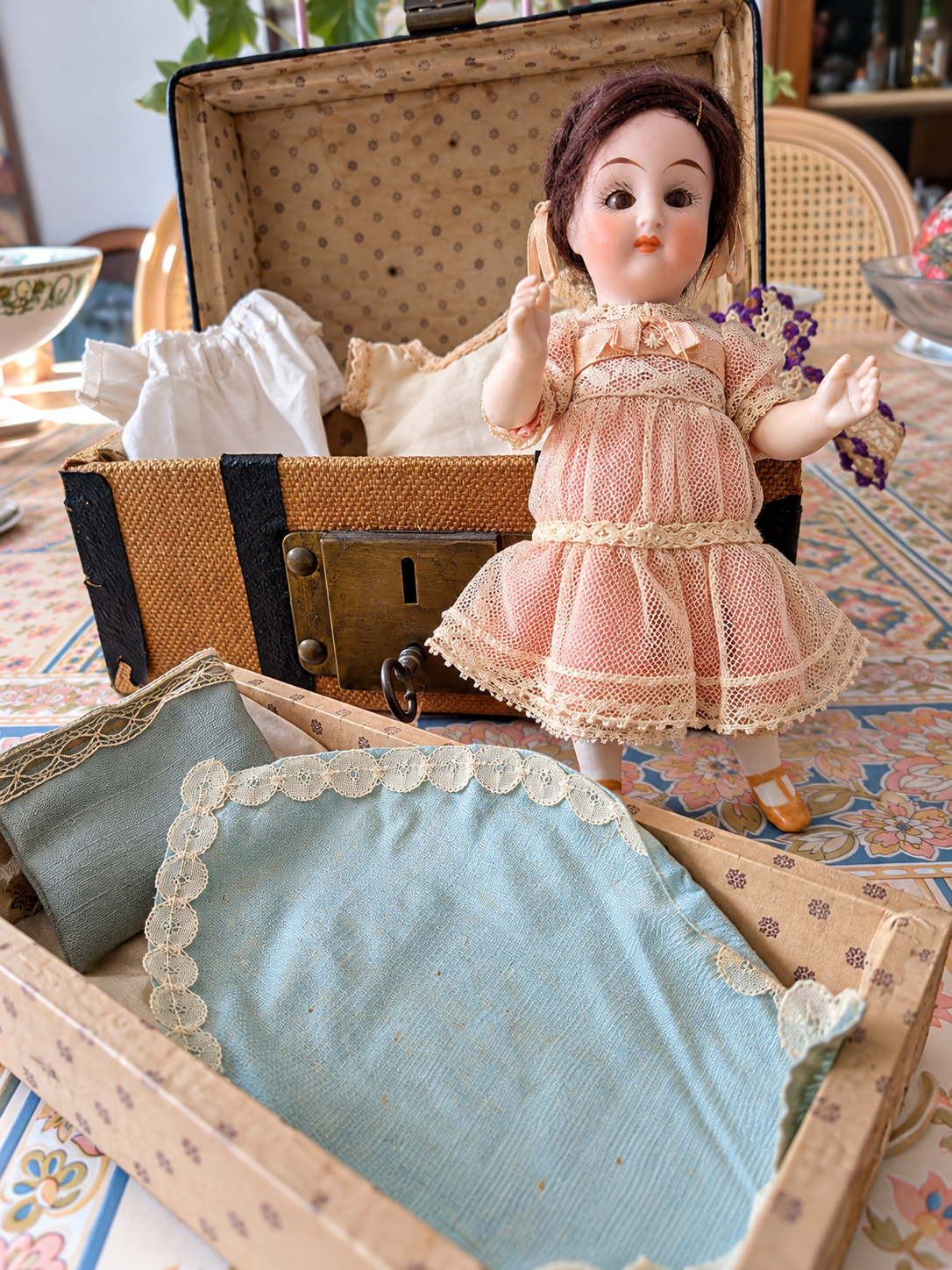 Mignonnette de 14 cm — mallette et trousseau — La mignonnette debout auprès de sa mallette ouverte, avec son petit lit et les vêtements du trousseau — vue 1.