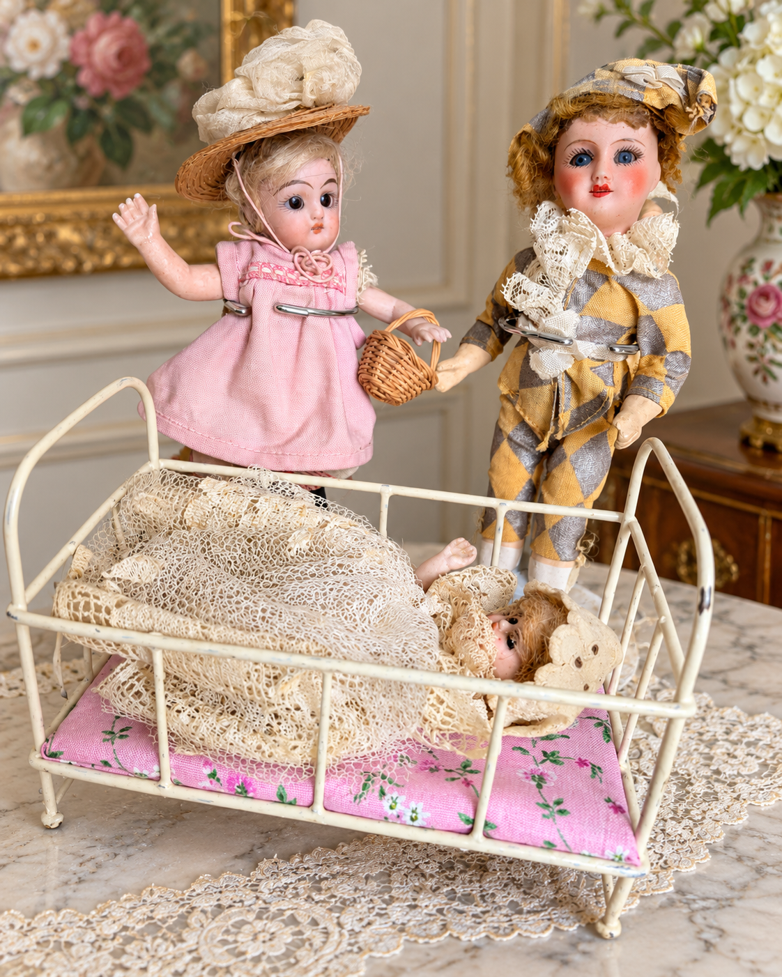 Mignonnettes anciennes : scènes et mobilier miniature — collection de Mireille (3/3) — La poupée en robe rose et le personnage en costume à losanges près du lit métallique blanc, avec une petite poupée sous la dentelle — vue 2.