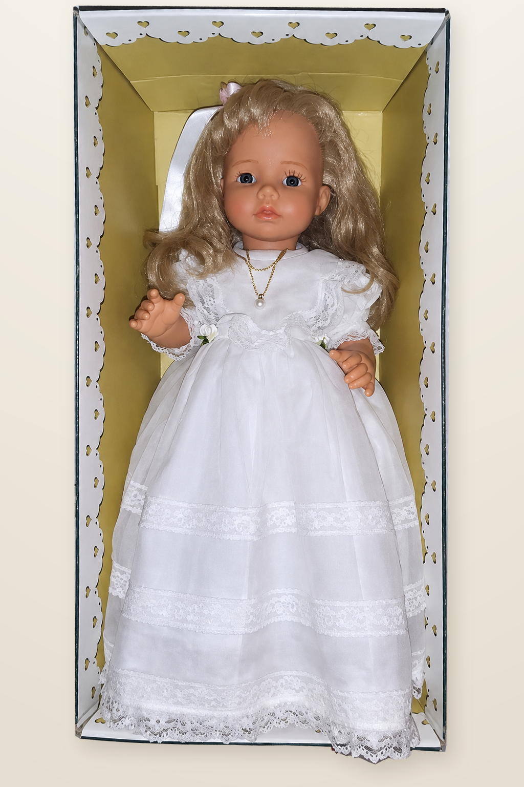 Paula en tenue de communion — Mariquita Pérez, Miel de Abeja — Paula, collection Miel de Abeja de Mariquita Pérez, en longue robe blanche de communion ornée de dentelles, avec ruban dans les cheveux et collier à pendentif, présentée dans une boîte à bordure découpée de cœurs — vue 1.
