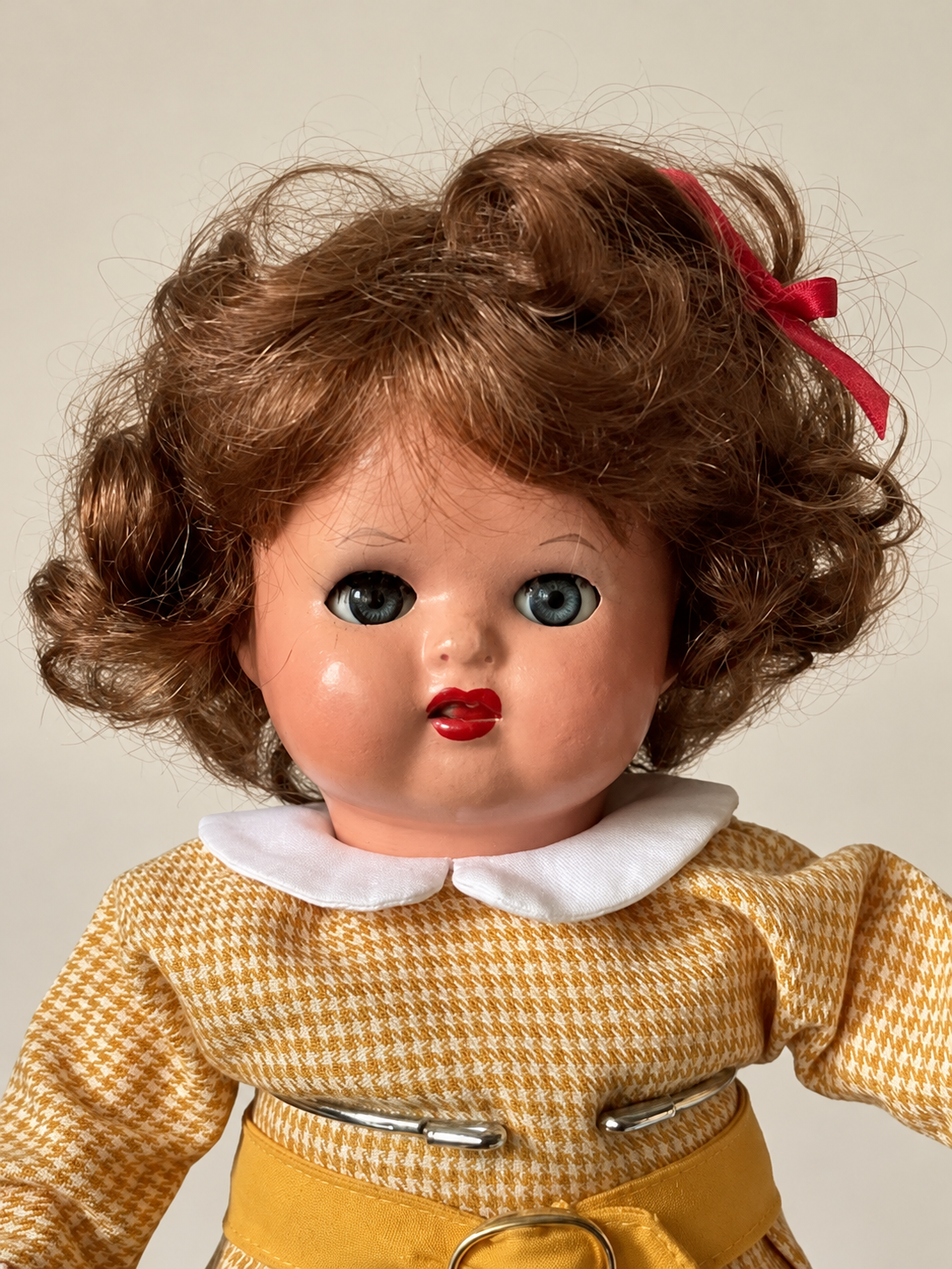 Une tête retrouvée, une poupée recréée — Femmes d’Aujourd’hui, collection de Françoise — Portrait de la poupée de Françoise après réparation : yeux bleus, joues roses, bouche rouge, perruque brune moderne et nœud rouge au-dessus du col blanc — vue 3.
