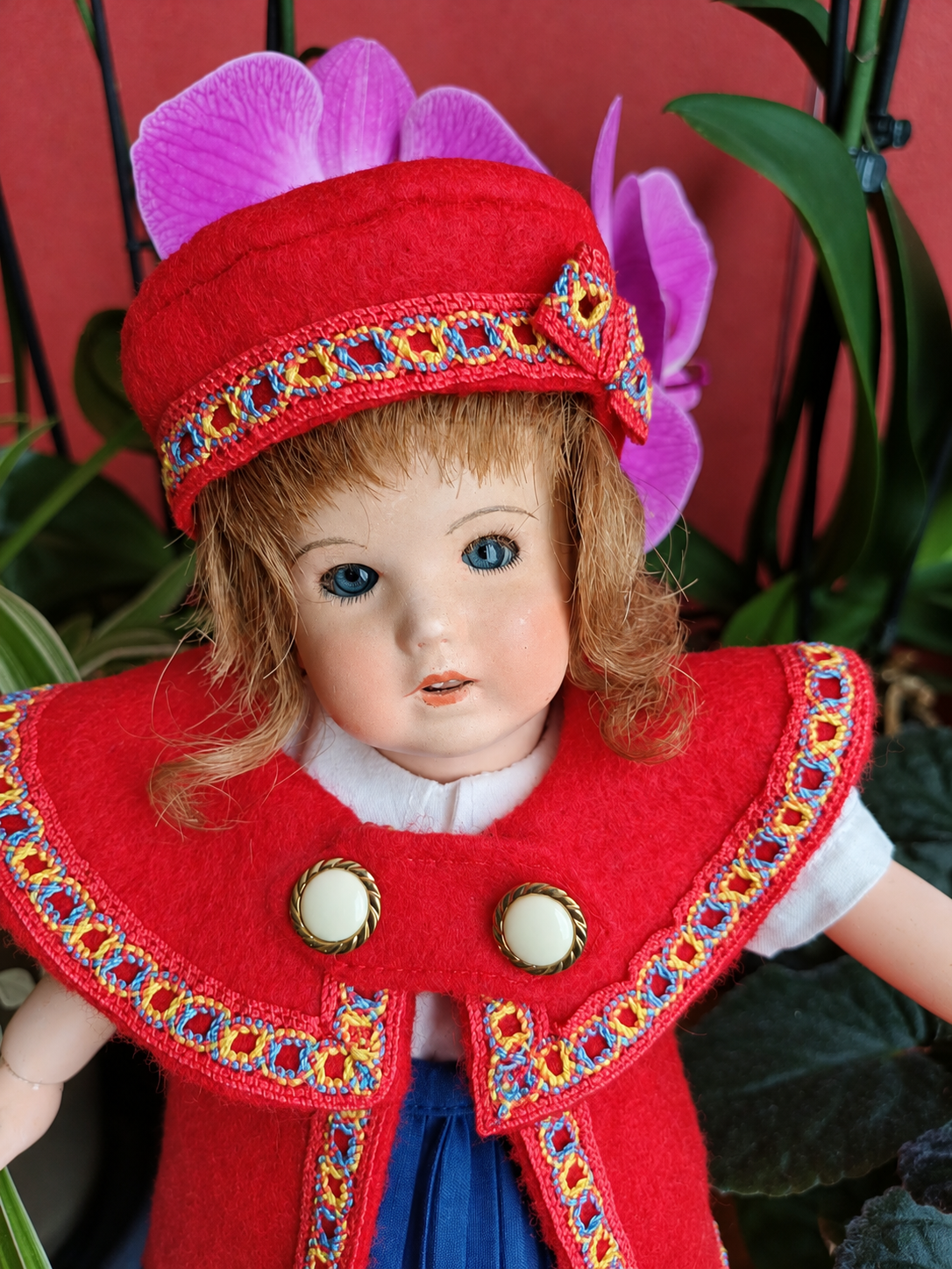Bleuette 251 — la nouvelle tenue rouge et bleue cousue par Françoise — Portrait rapproché de Bleuette 251 : yeux bleus, cheveux clairs et chapeau rouge assorti aux bordures multicolores de sa nouvelle tenue — vue 4.