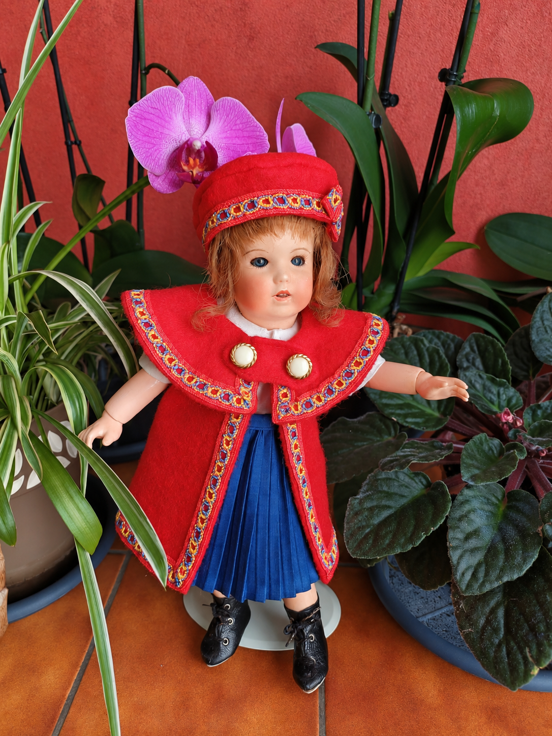 Bleuette 251 — la nouvelle tenue rouge et bleue cousue par Françoise — Vue d’ensemble de la Bleuette 251 de Françoise, en nouvelle tenue rouge et bleue avec chapeau assorti et bottines noires, parmi les plantes — vue 1.