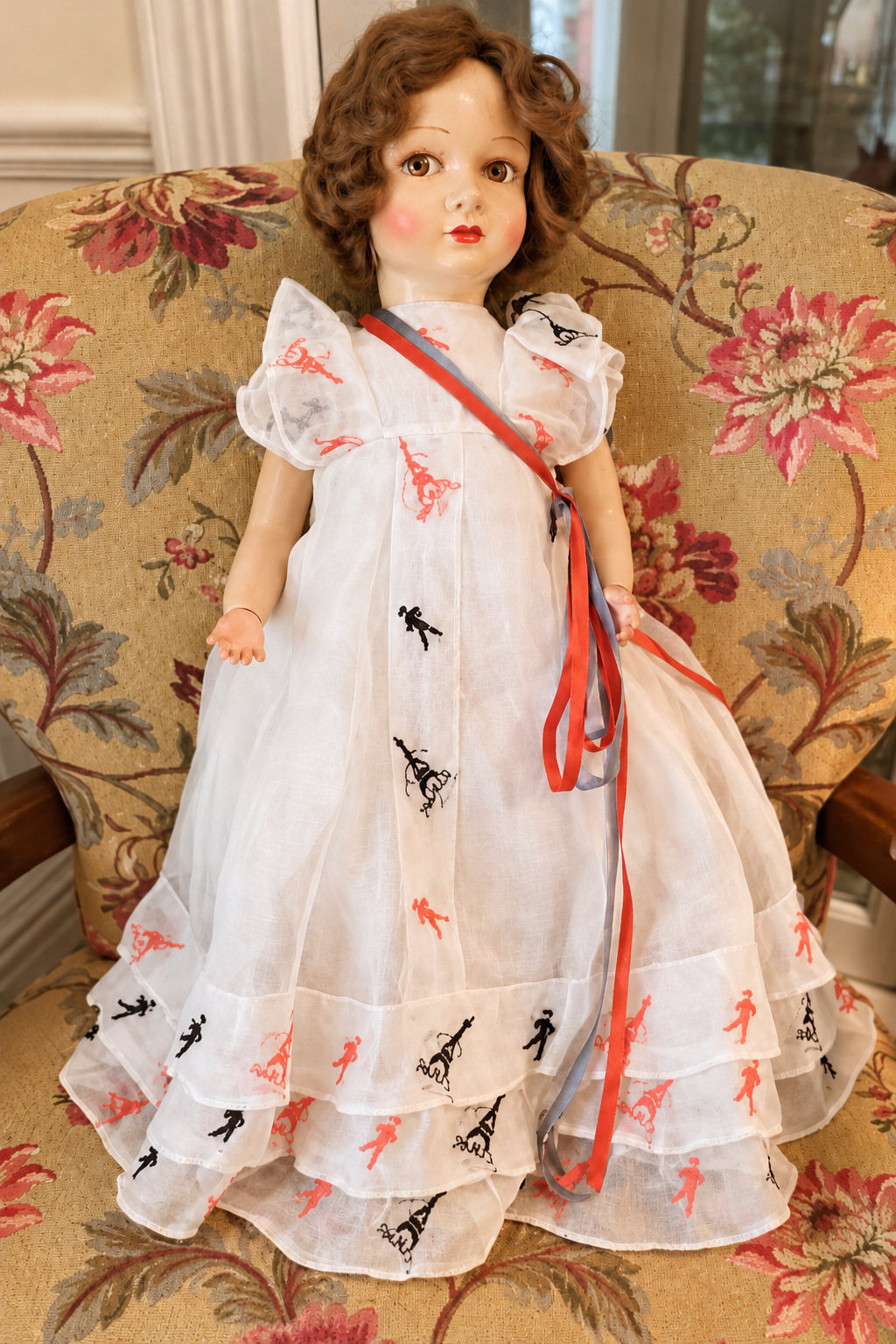 Vénus en étoffe — robe blanche à motifs — La poupée Vénus présentée par Christine, en robe blanche à motifs rouges et noirs, sur un fauteuil fleuri — vue 1.