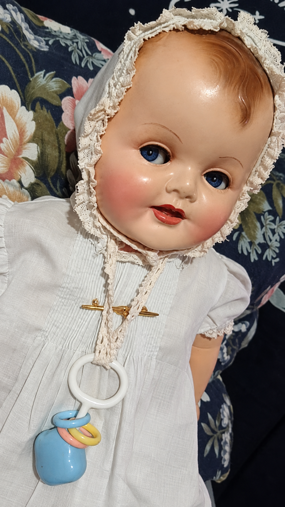 Gros bébé Raynal — présentation de Lydia — Détail du bonnet de dentelle, de la robe blanche plissée et du petit accessoire à anneaux colorés — vue 3.