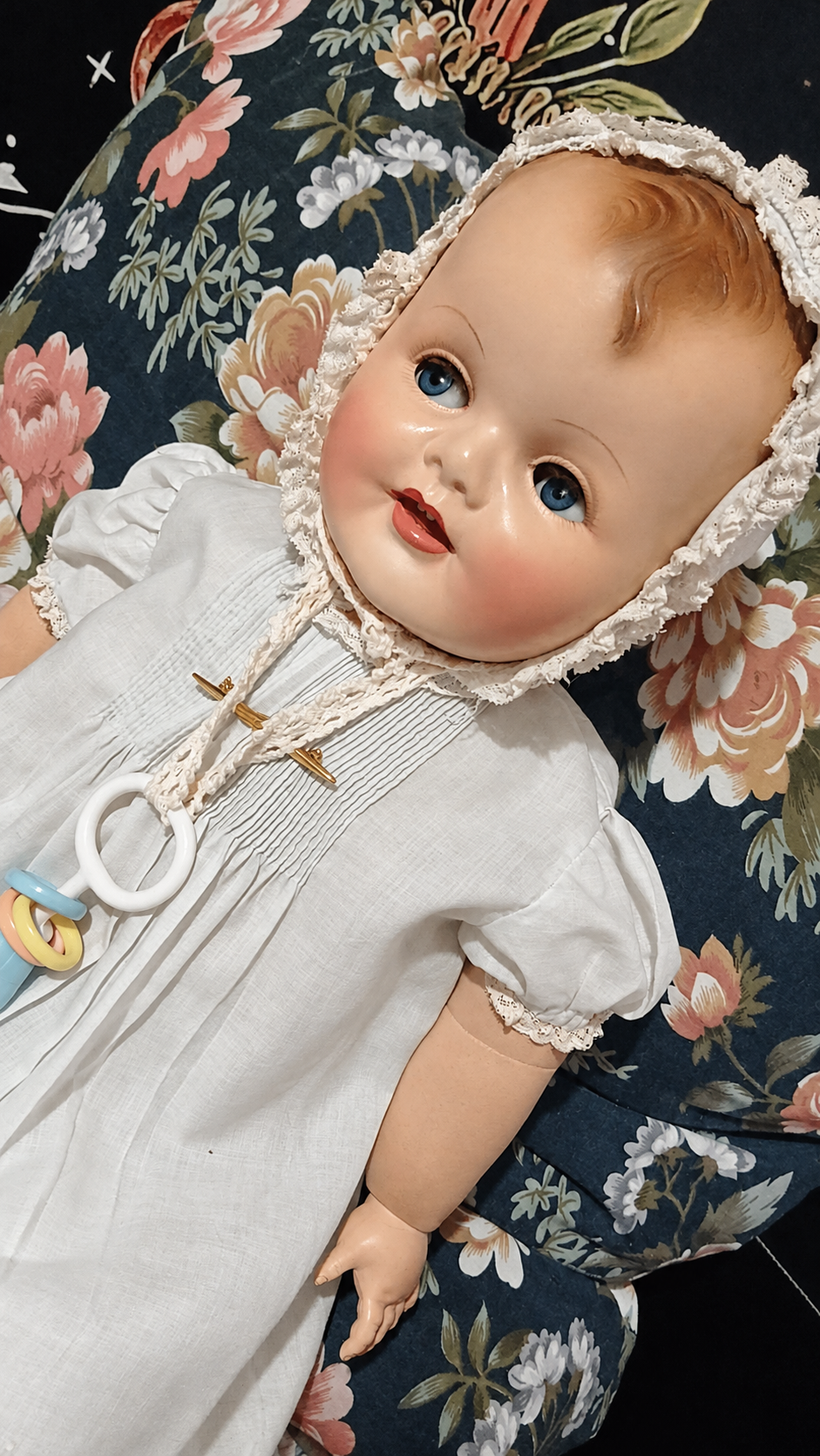 Gros bébé Raynal — présentation de Lydia — Le bébé de Lydia allongé sur un coussin fleuri, en robe blanche et bonnet bordé de dentelle — vue 1.